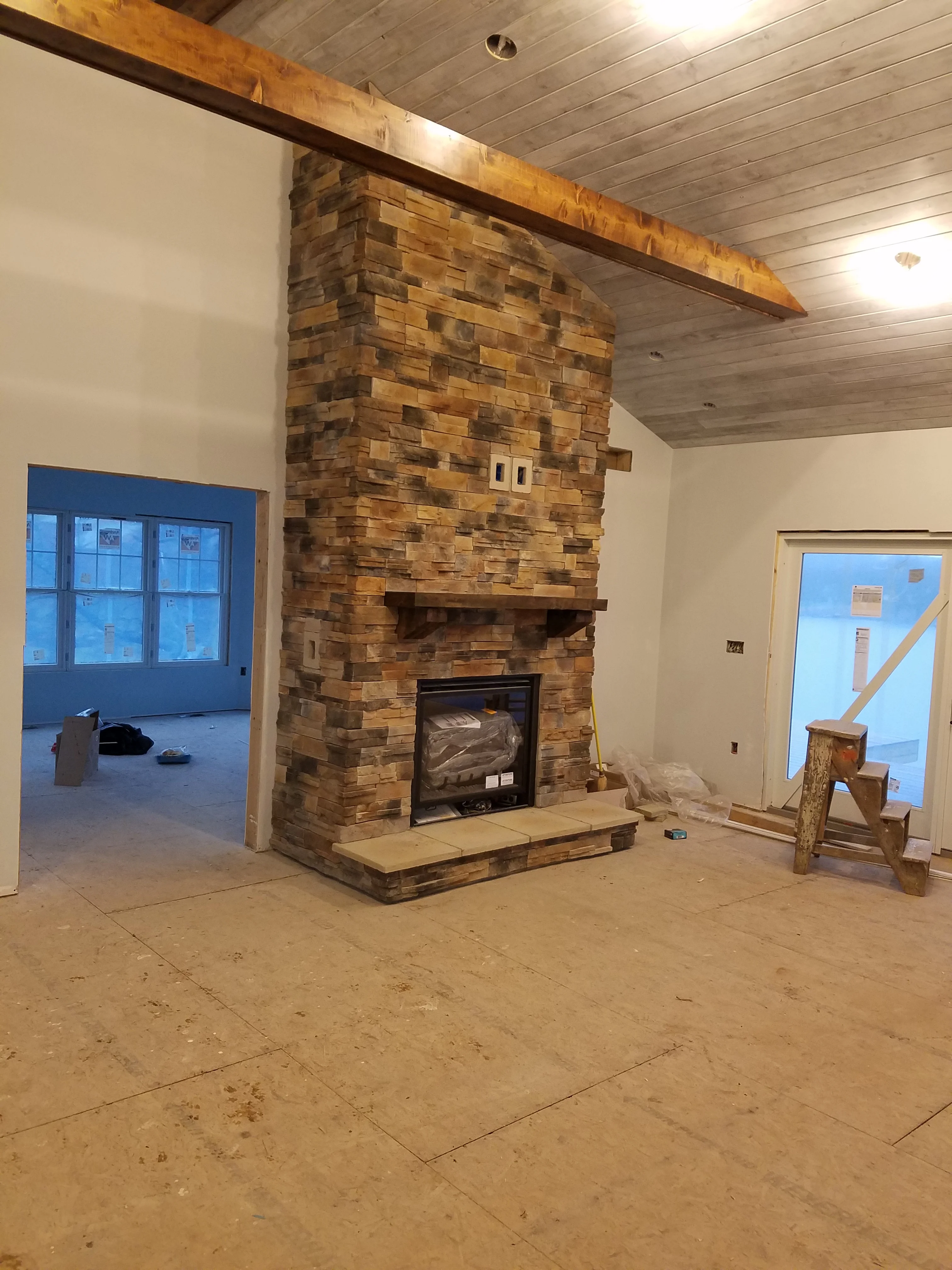 Stacked stone fireplace with timber mantel beam and gas insert in construction phase