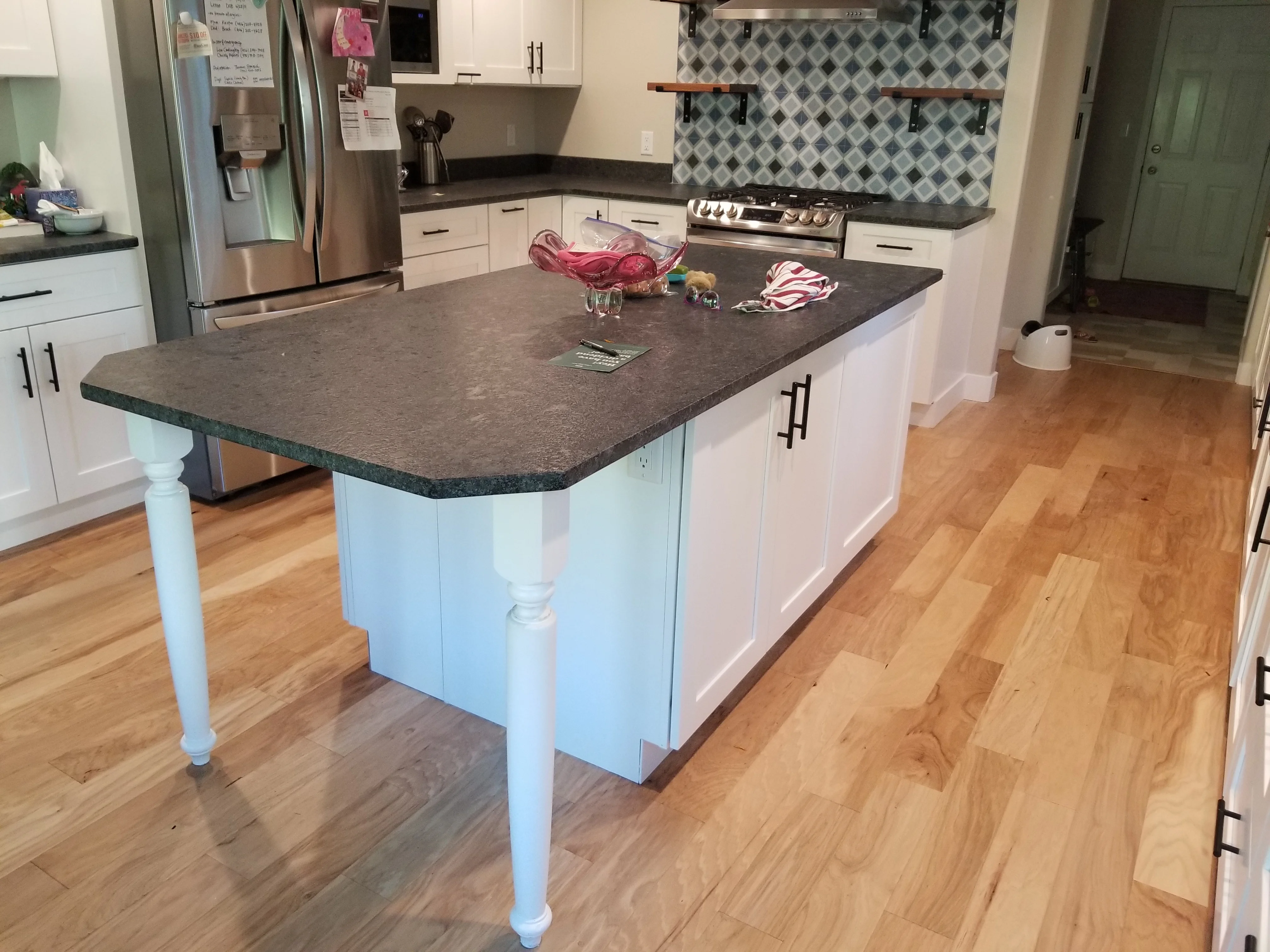 Kitchen island with blue base, dark quartz top, white cabinetry, geometric tile backsplash, and hardwood floors