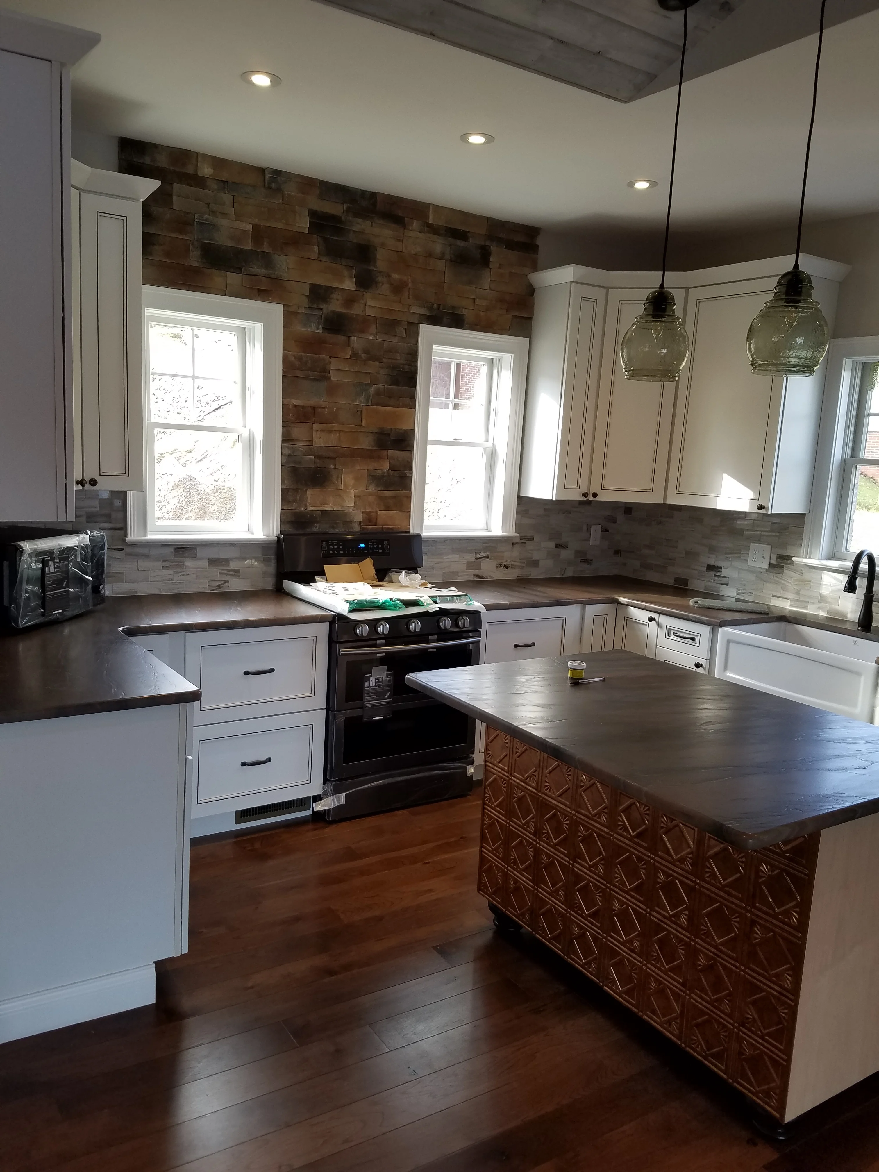 Kitchen with white cabinets, stone backsplash, dark wood island, and pendant lighting