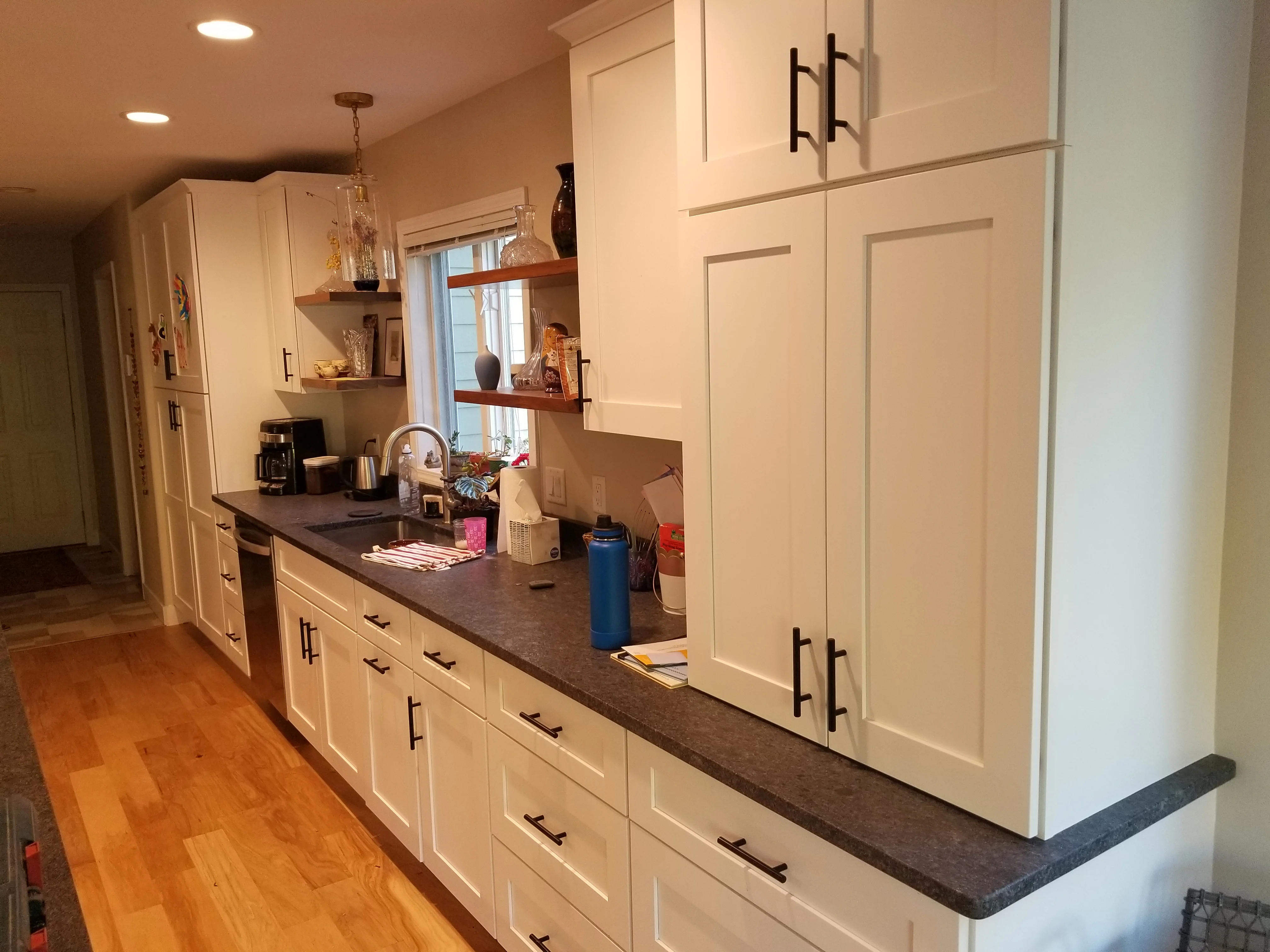 White kitchen cabinets with dark quartz countertops and floating wood shelves