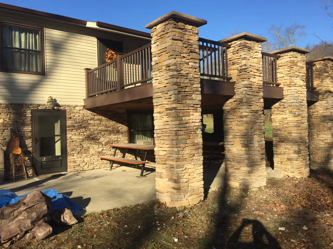 Stacked stone pillars with metal railings, composite deck, and horizontal siding on residential addition