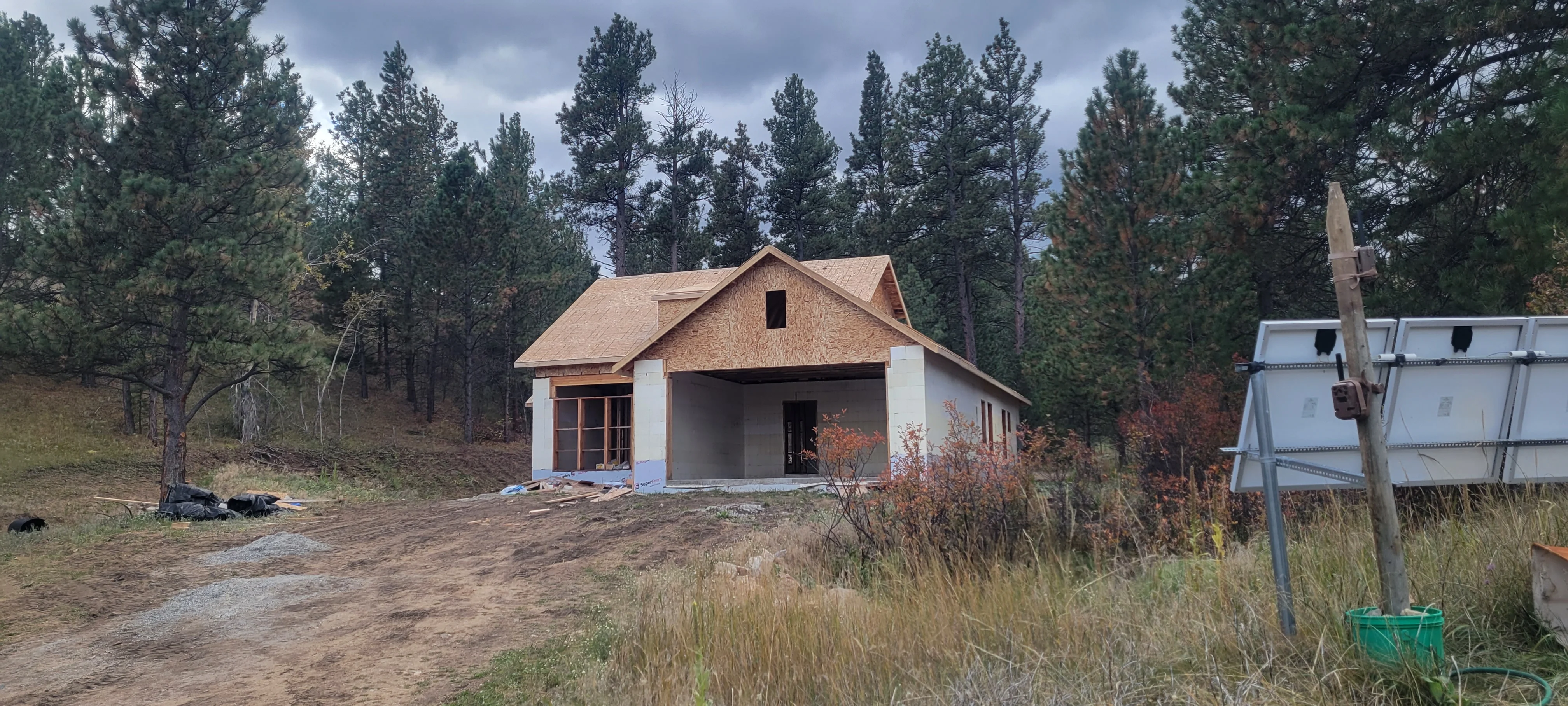 New home construction with white walls, brown roof, covered porch, and solar panels in forest setting