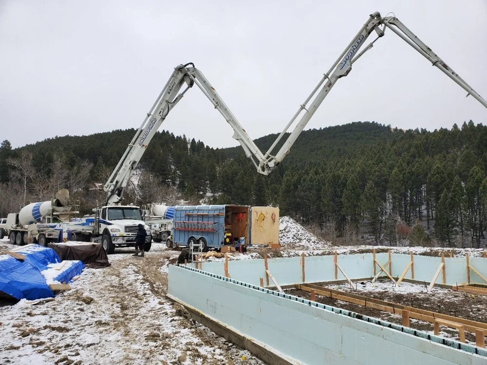Dual concrete pump trucks pouring foundation with perimeter wall and wooden bracing