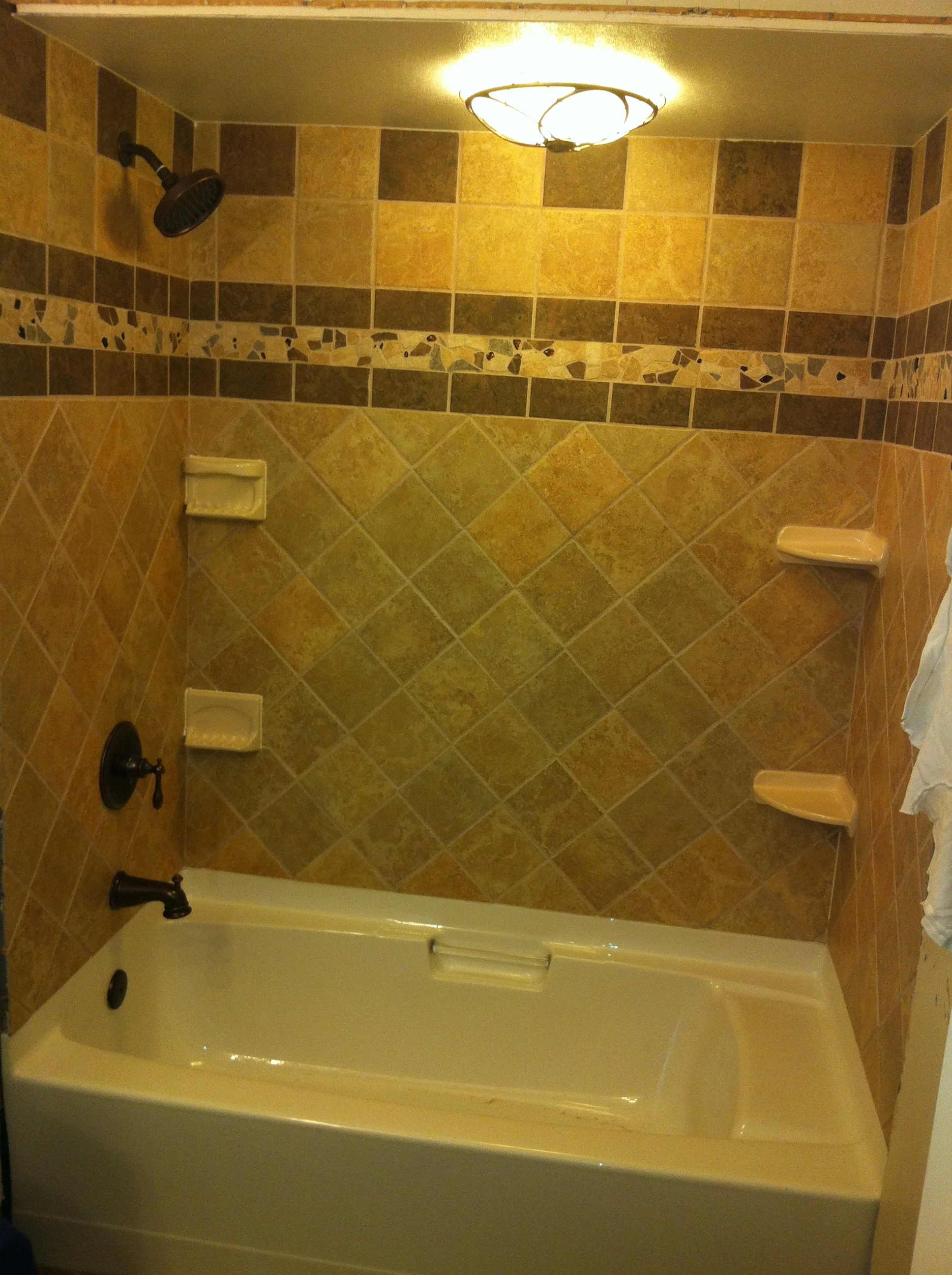Bathroom shower surround with diagonal ceramic tile, decorative border, and built-in shelves