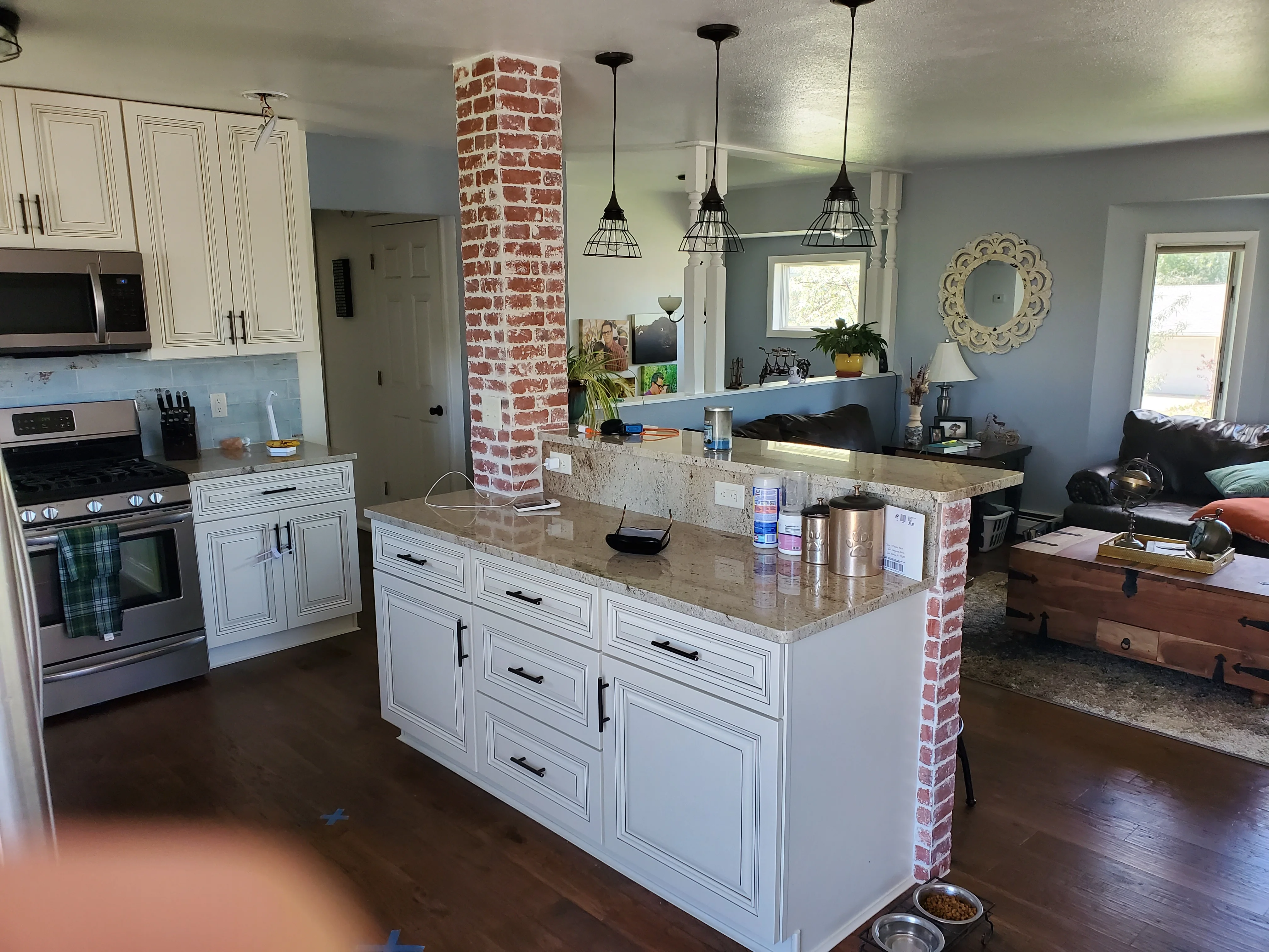 White kitchen cabinetry with granite counters, stainless appliances, exposed brick column, and pendant lighting
