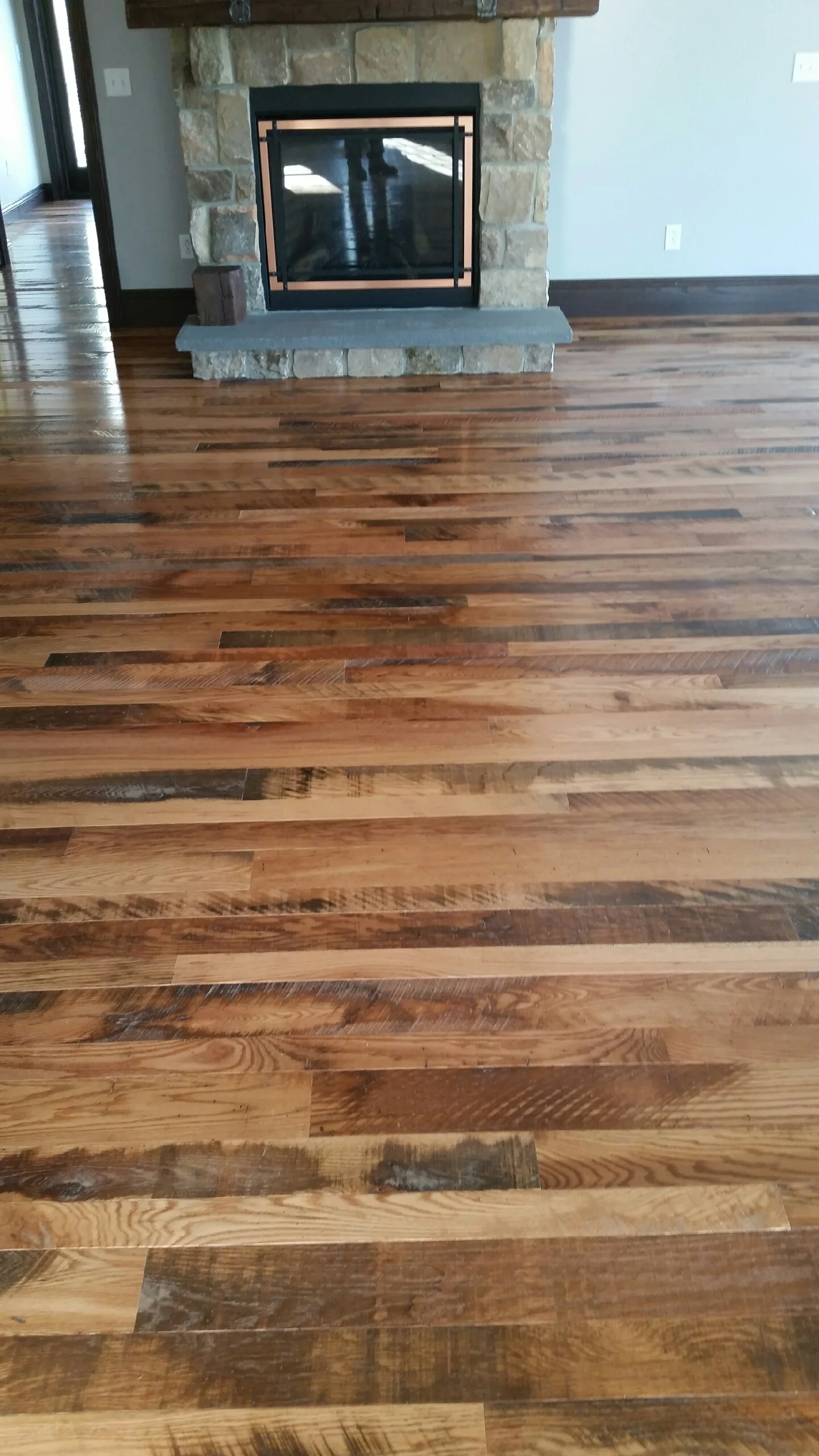 Mixed-width hardwood flooring with varied wood tones installed in living room with stone fireplace