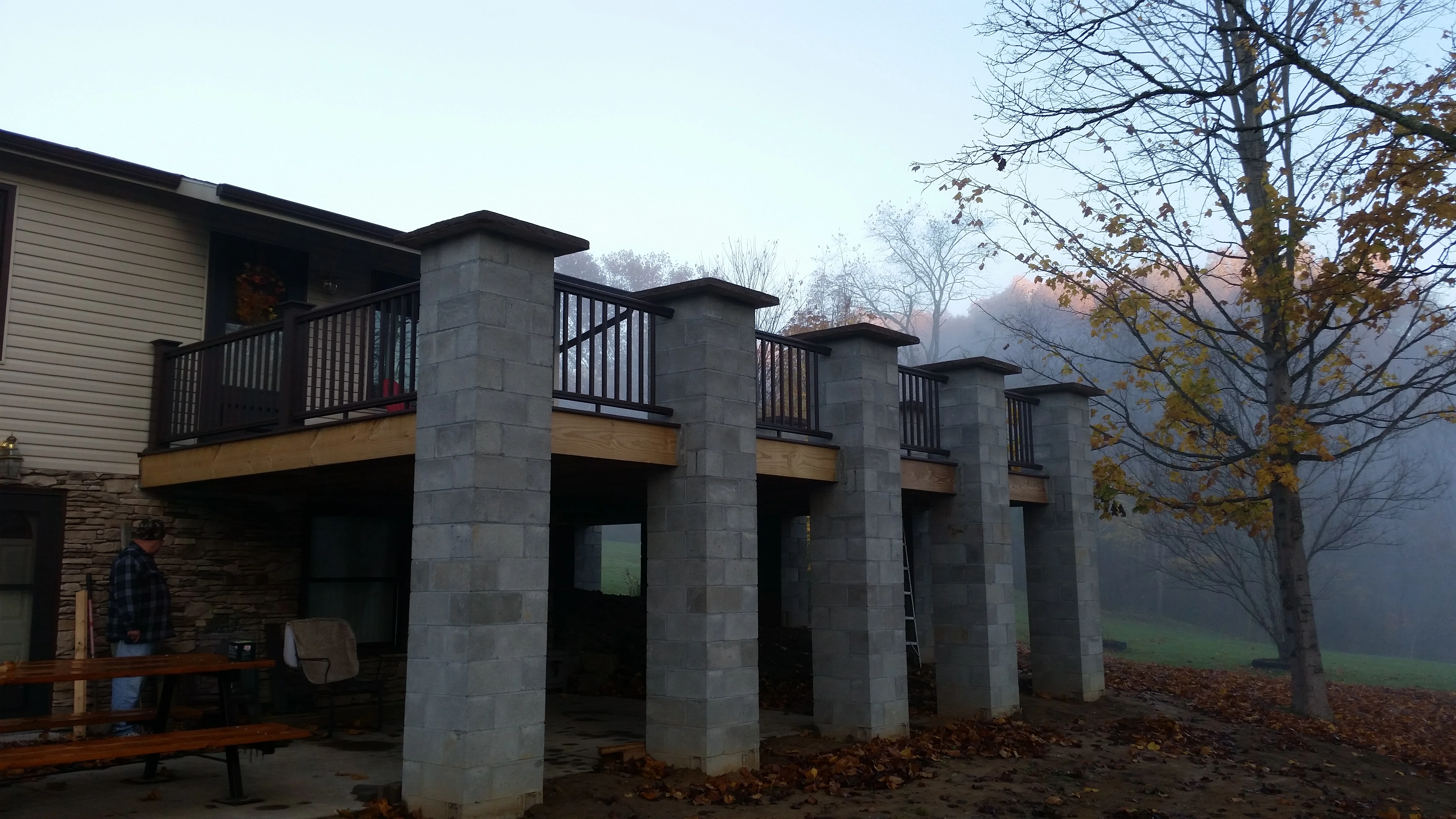 Elevated multi-level deck with black railings, concrete pier supports, and covered patio underneath