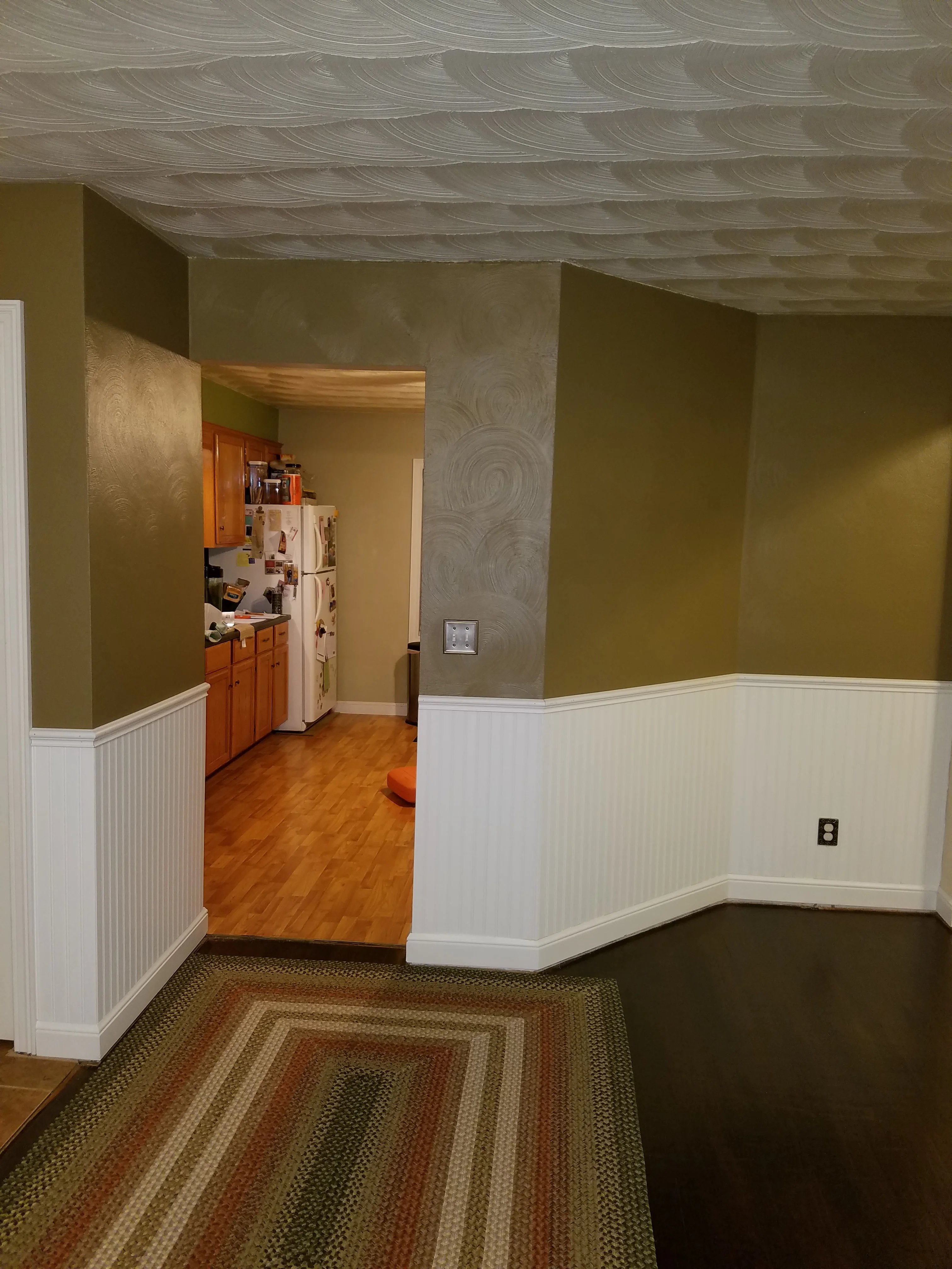 Basement with textured ceiling, olive walls, white wainscoting, and hardwood flooring