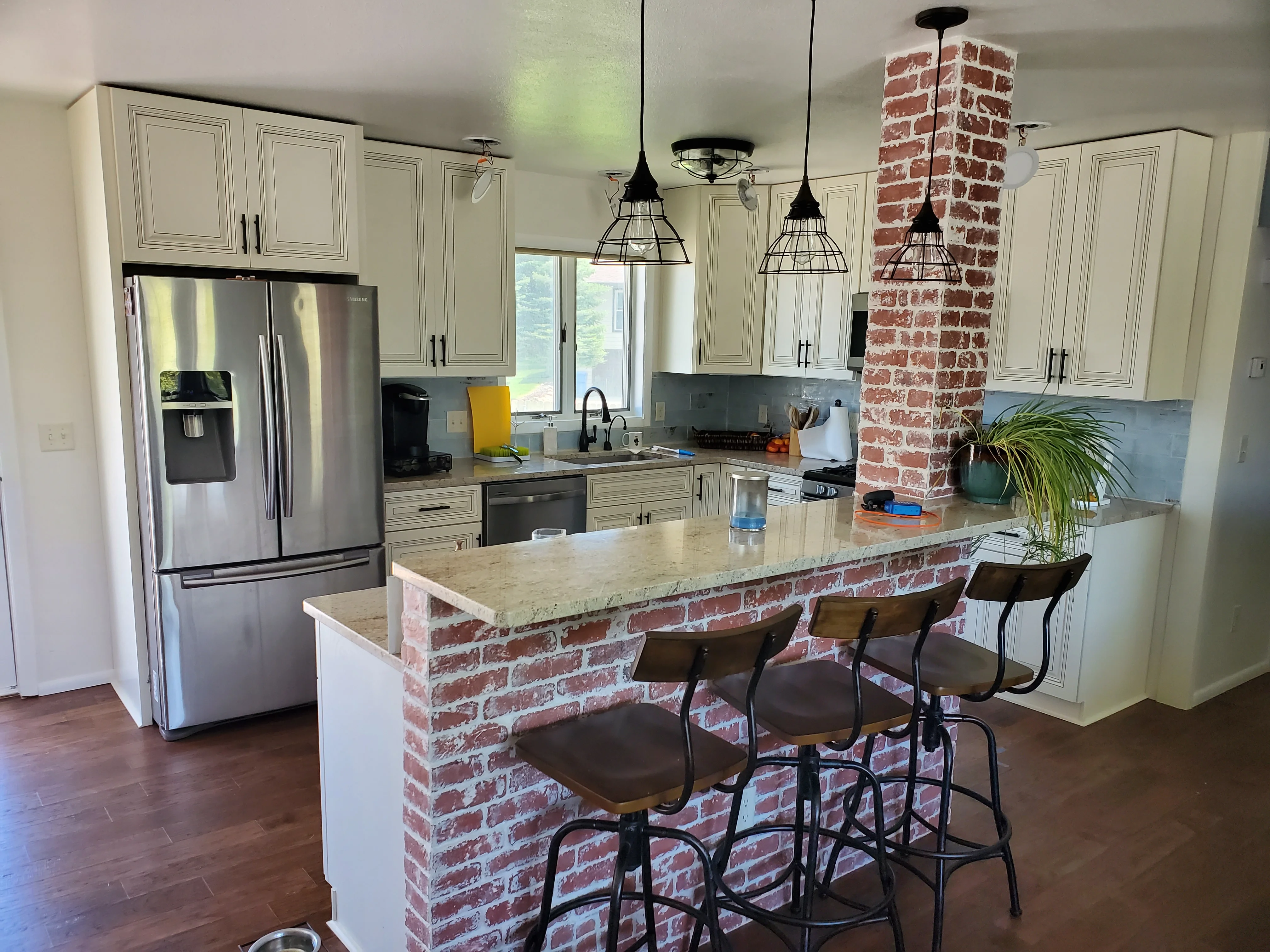 Kitchen with cream cabinets, stainless appliances, exposed brick island with quartz top, and pendant lighting