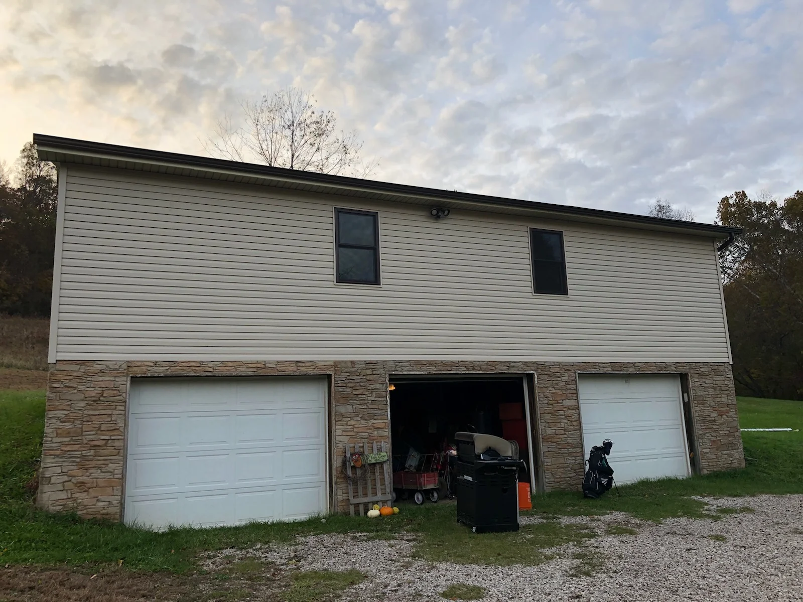Light gray vinyl siding and stacked stone veneer on residential garage structure with white garage doors