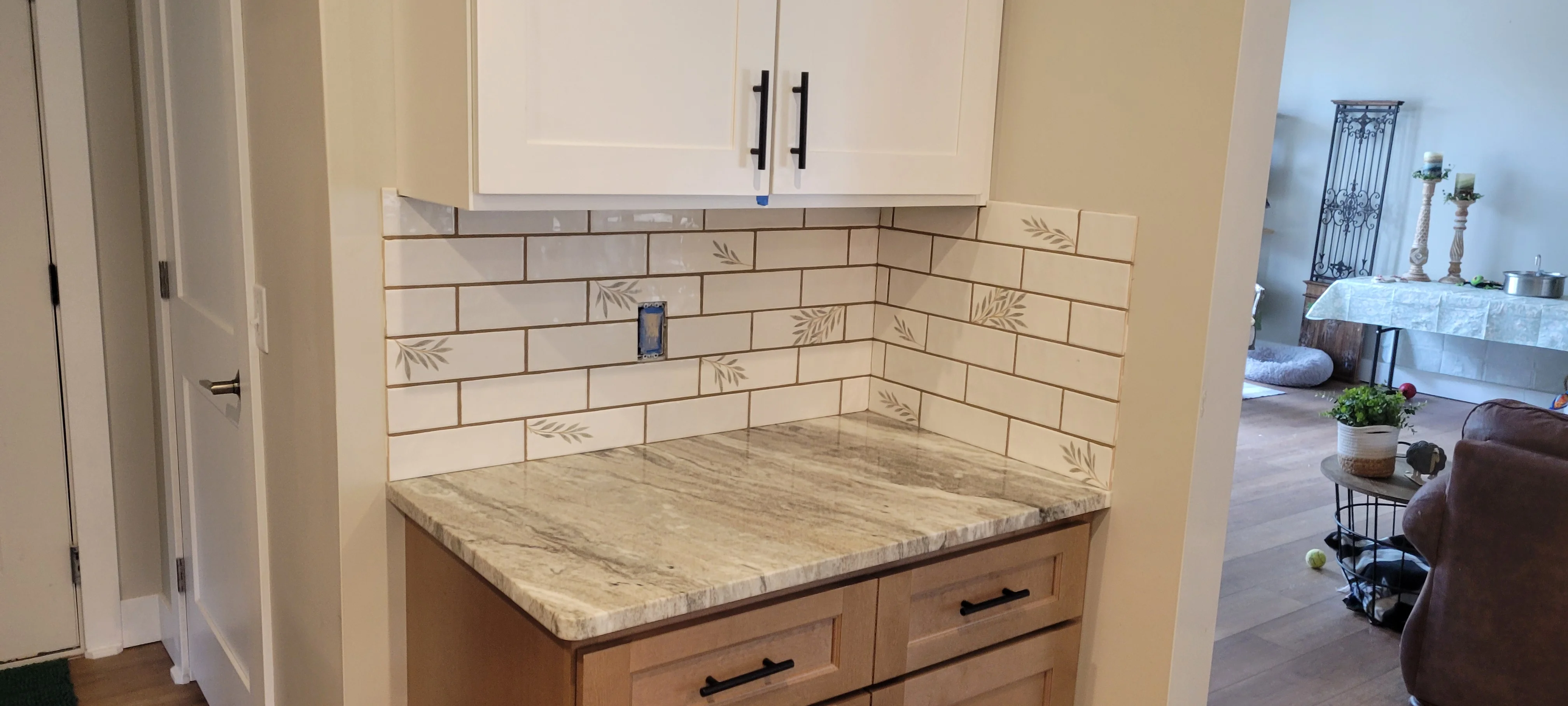 Cream subway tile backsplash with leaf pattern and travertine countertop over wood cabinetry