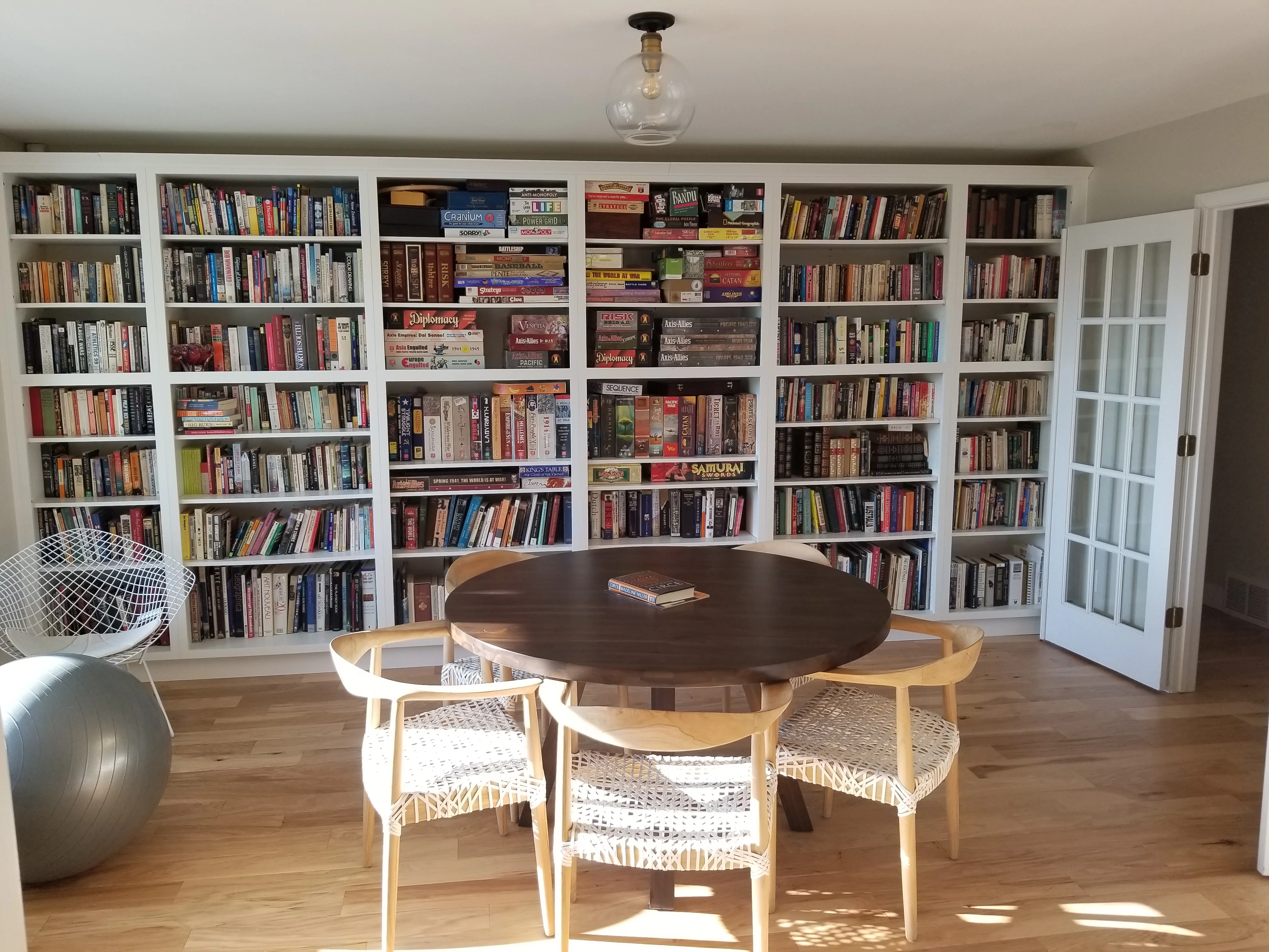 White built-in shelving with adjustable shelves, glass-door cabinets, and hardwood flooring in library room