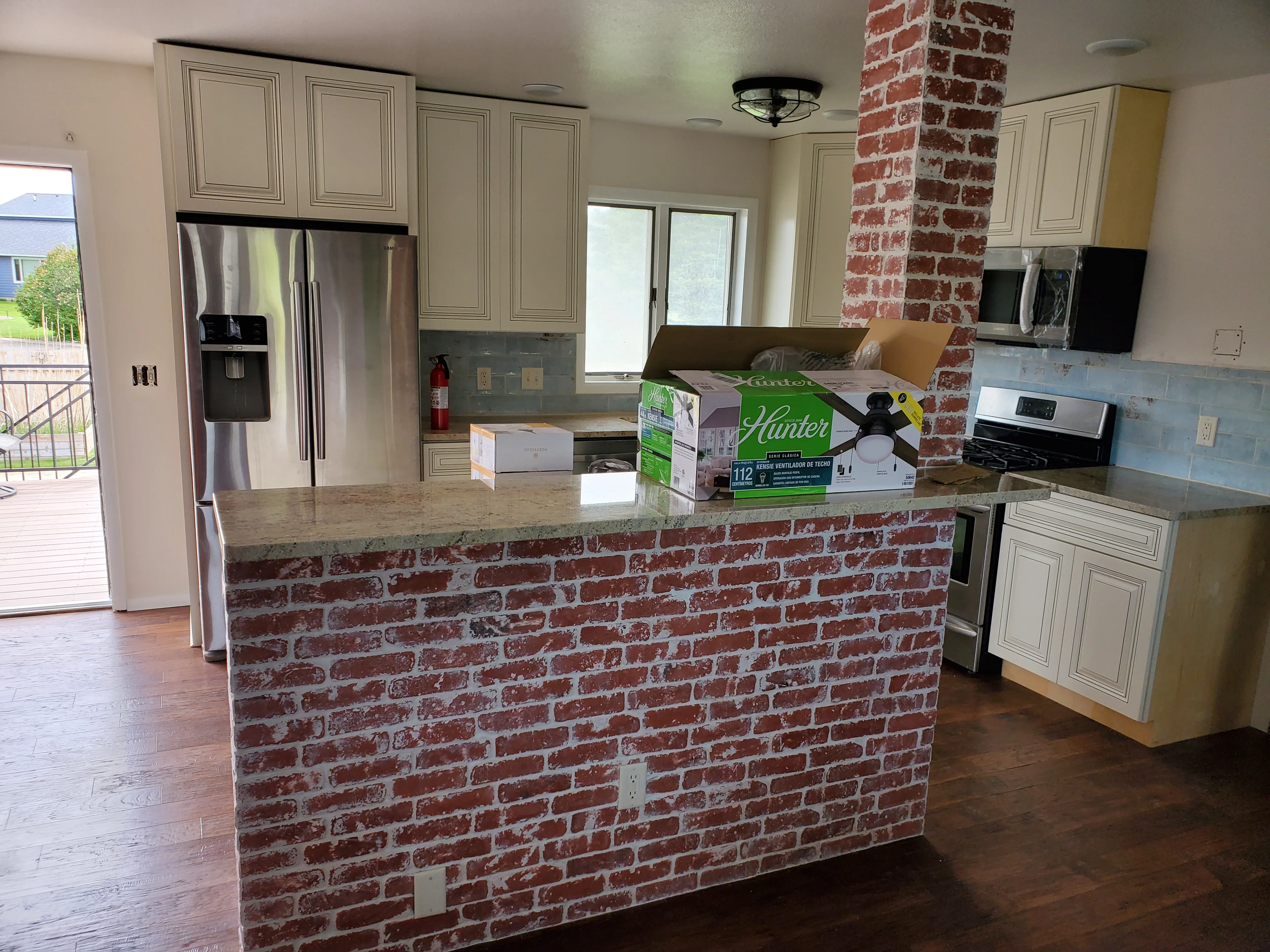 Kitchen with cream cabinetry, stainless steel appliances, exposed red brick island with quartz top