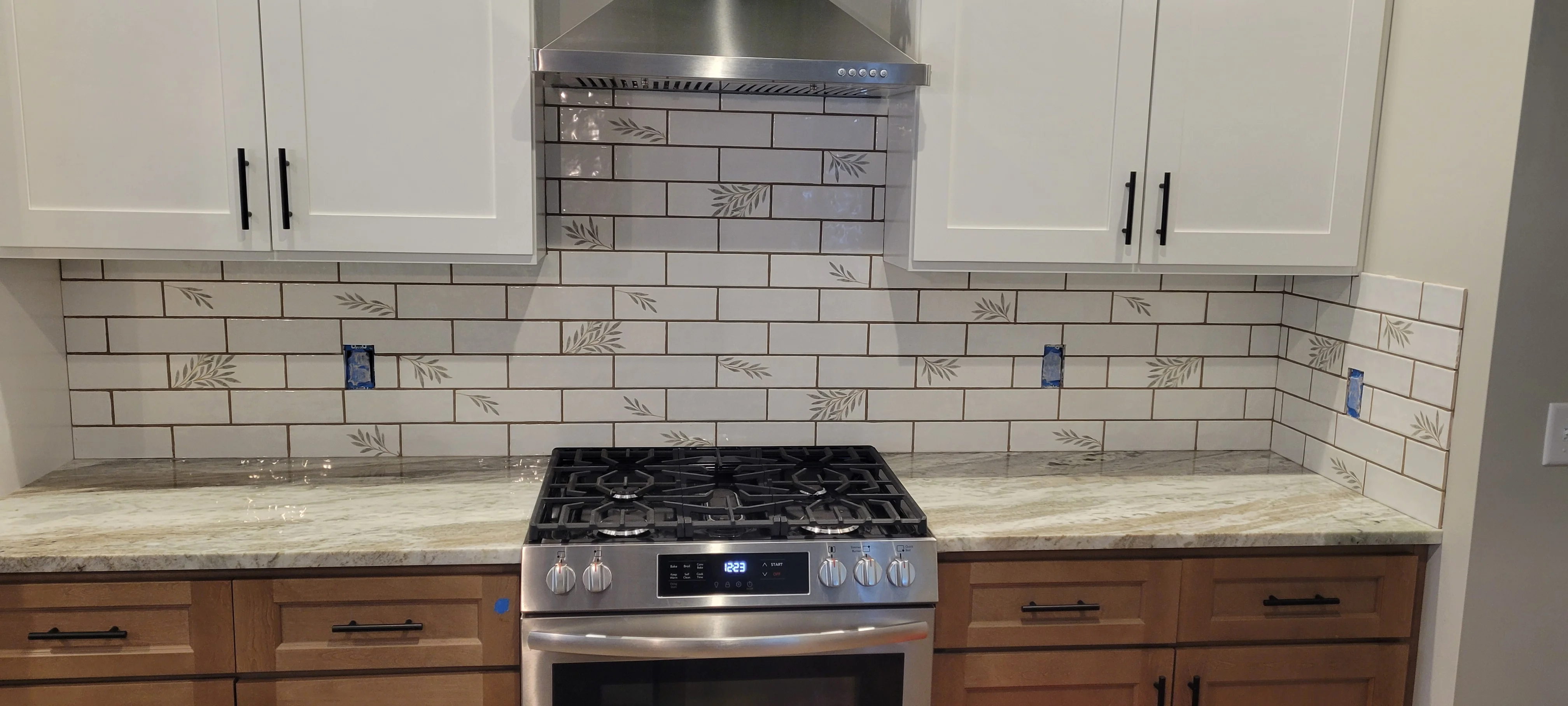 Subway tile backsplash with leaf pattern, marble countertops, stainless steel appliances, white and wood cabinetry