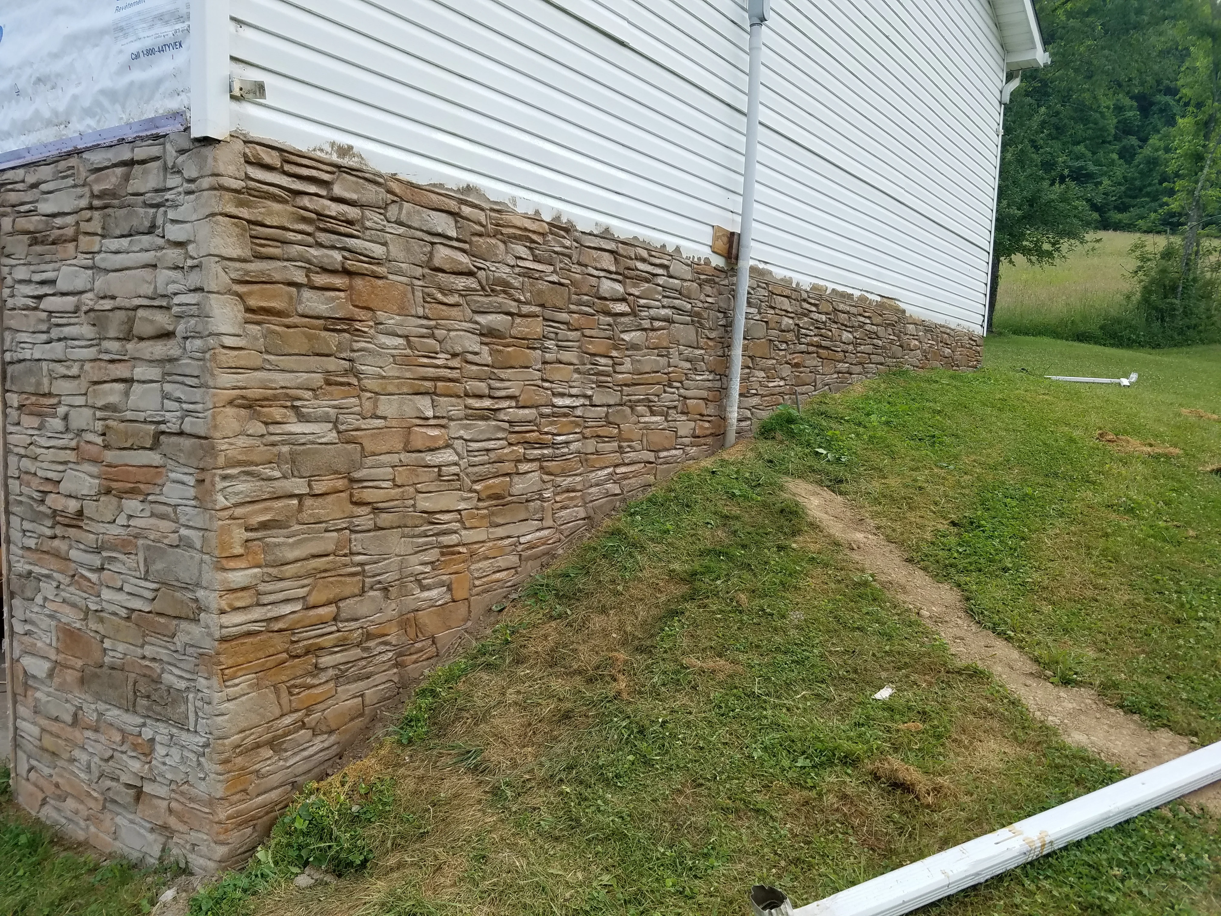 Stacked stone foundation wall with tan and brown stone blocks installed on residential home exterior