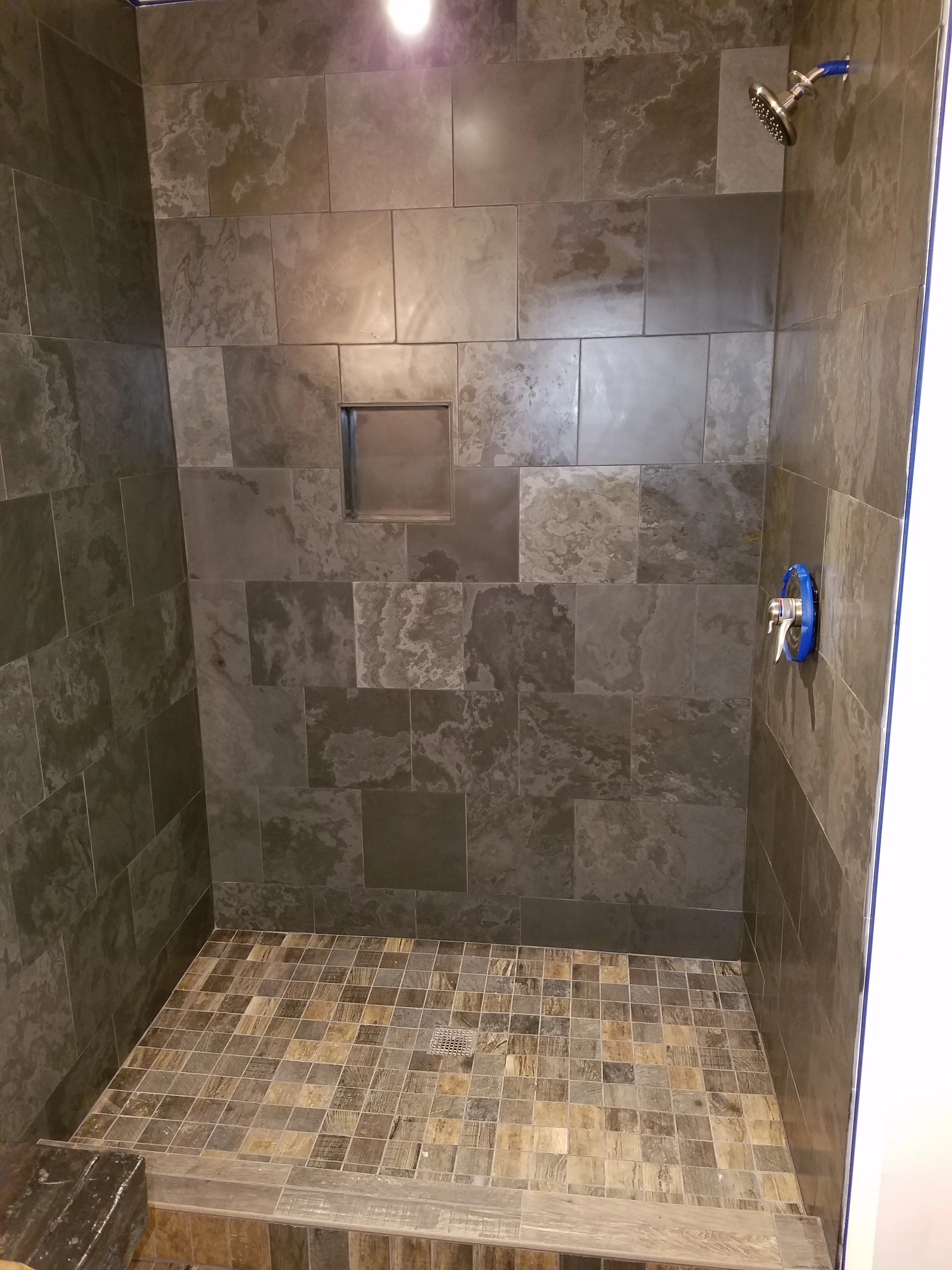 Tiled shower enclosure with porcelain wall tiles and mosaic floor tiles, rainfall showerhead, and recessed niche