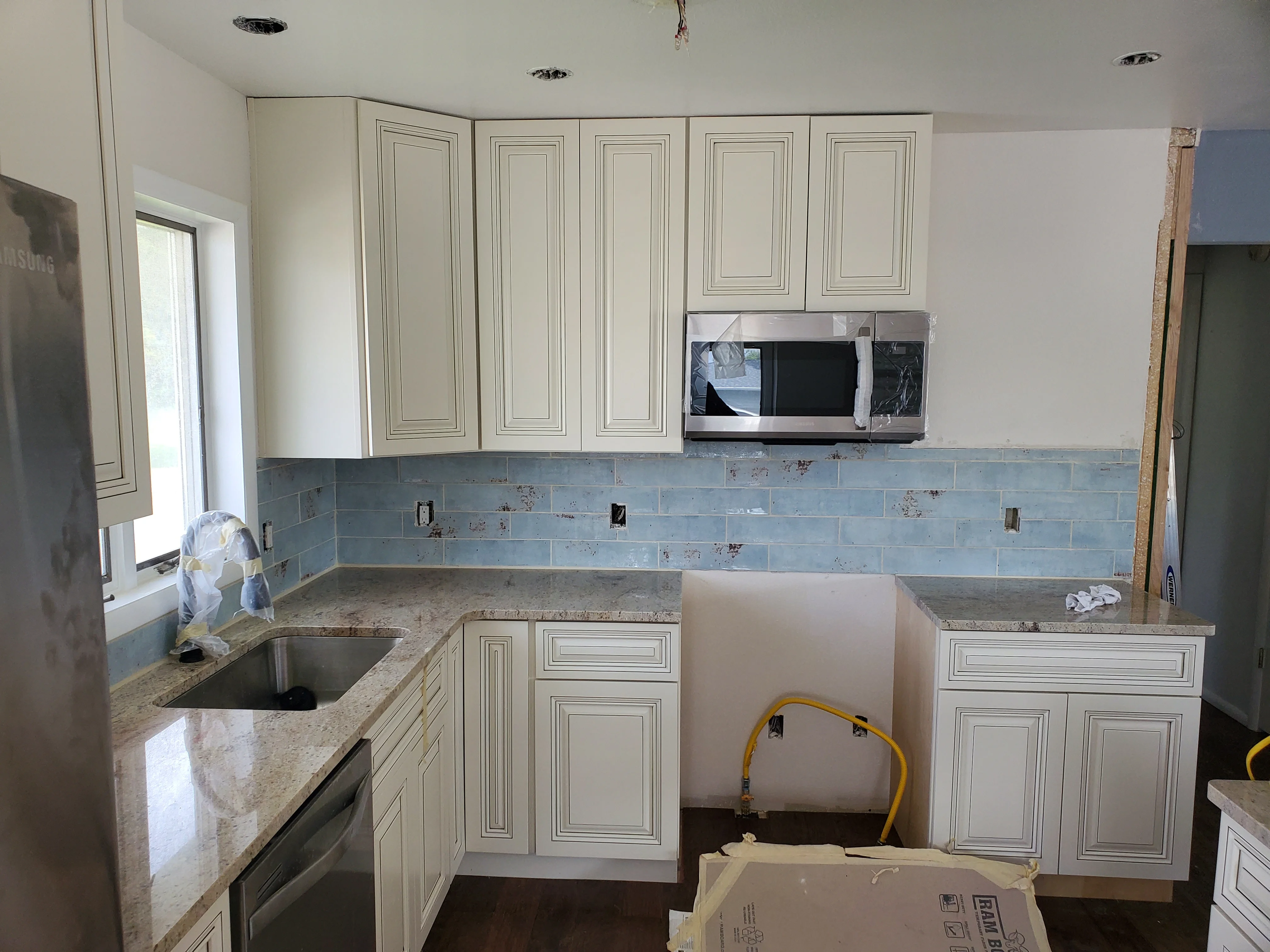 Kitchen with cream cabinetry, granite counters, and blue subway tile backsplash during installation