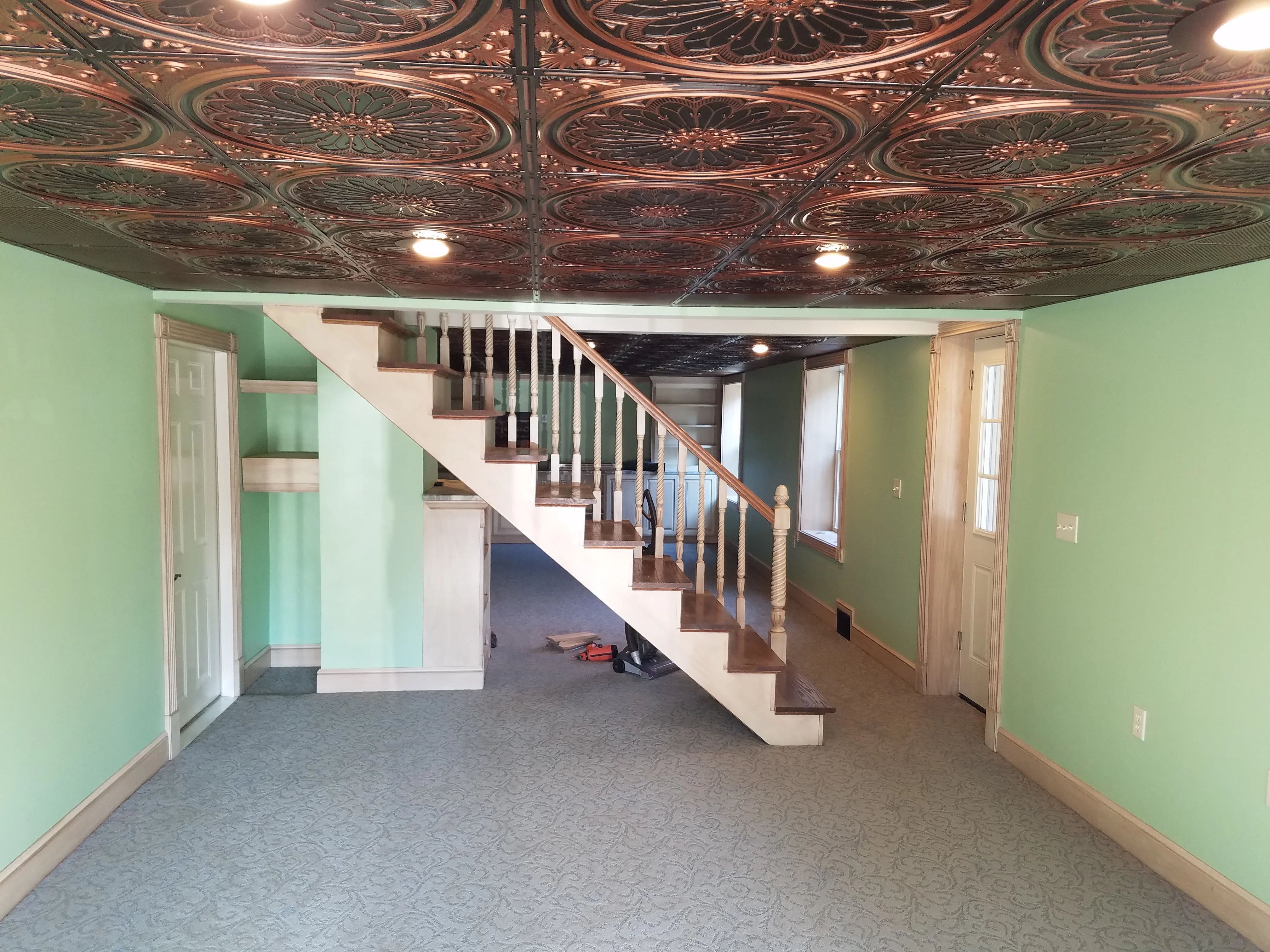 Finished basement with decorative copper ceiling tiles, wooden staircase, and green painted walls
