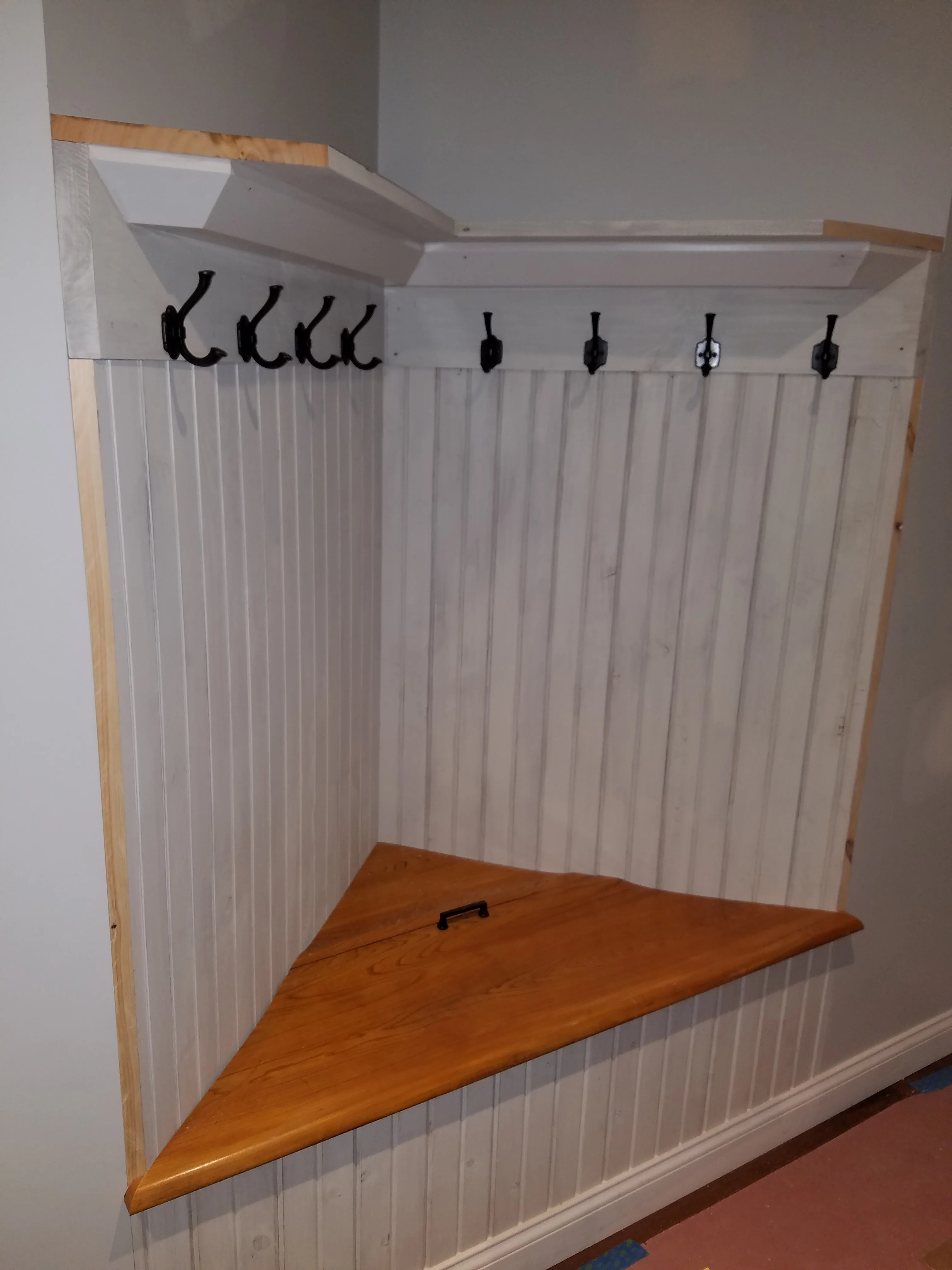 Triangular wood shelf with white beadboard backing and black hooks in corner installation