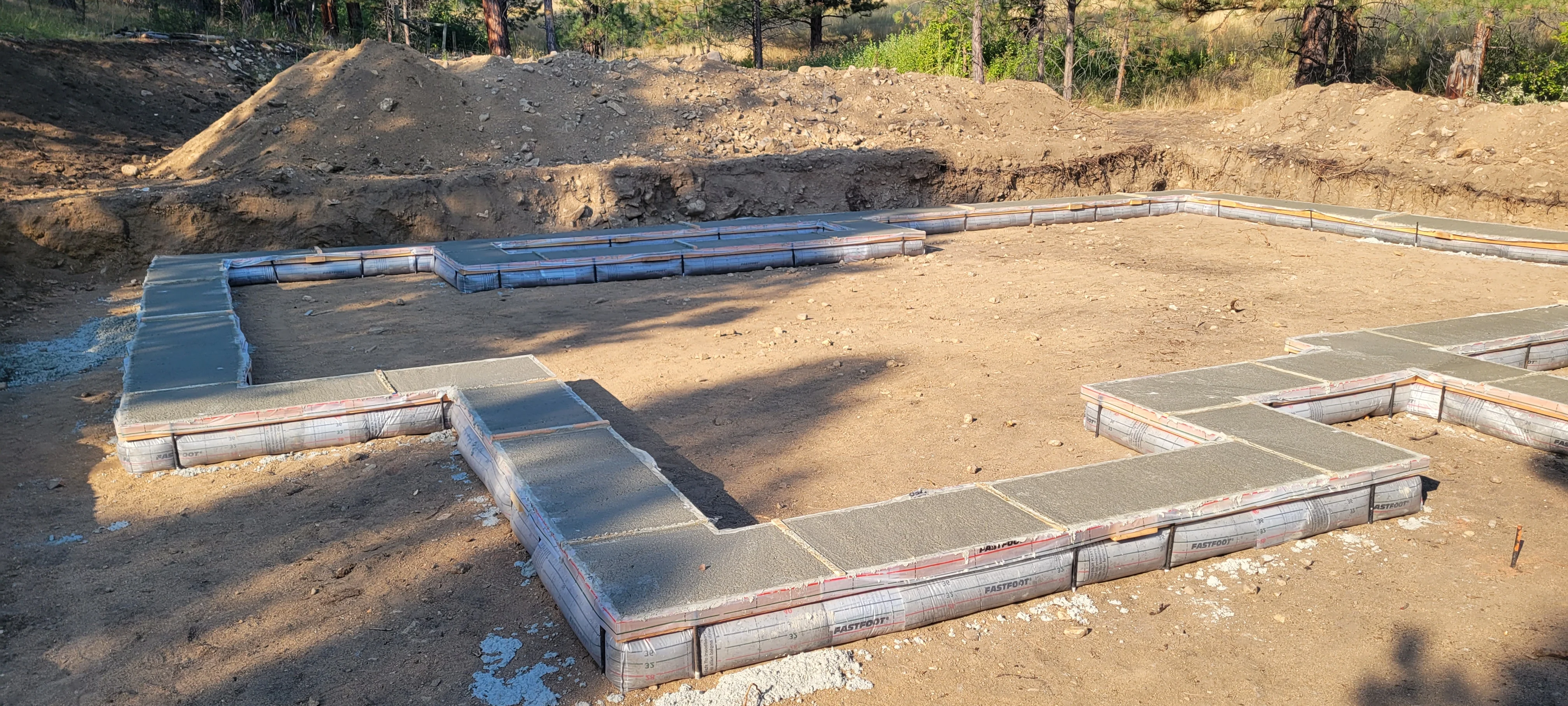 Concrete foundation footings and stem walls with blue protective sheeting on prepared soil base
