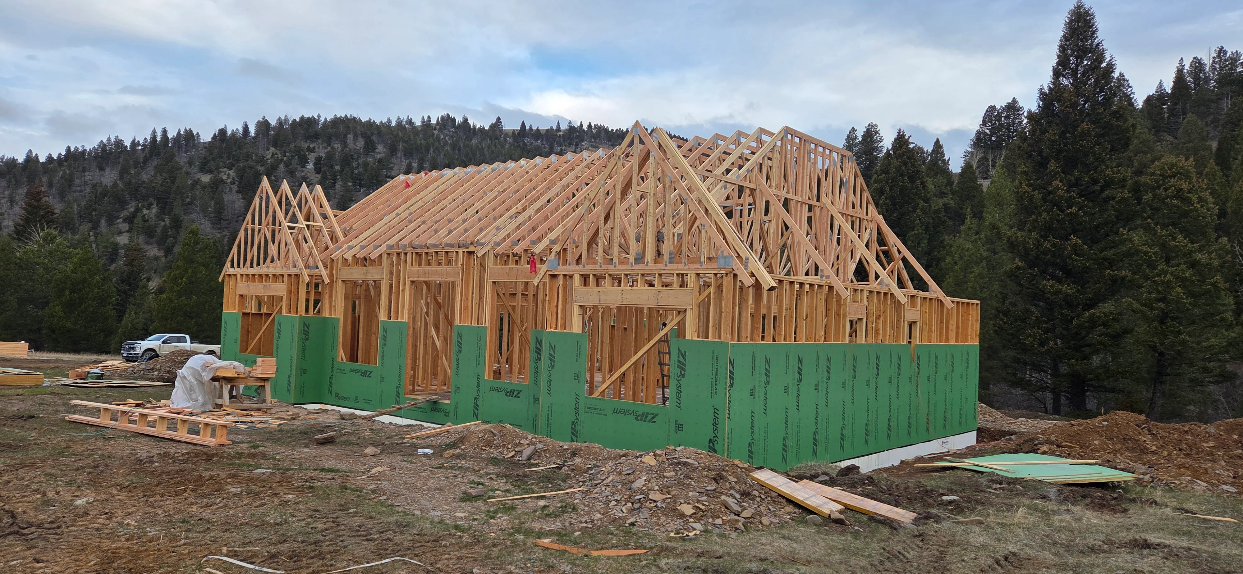 Timber frame home with exposed wood framing, green house wrap, and pitched roof trusses under construction