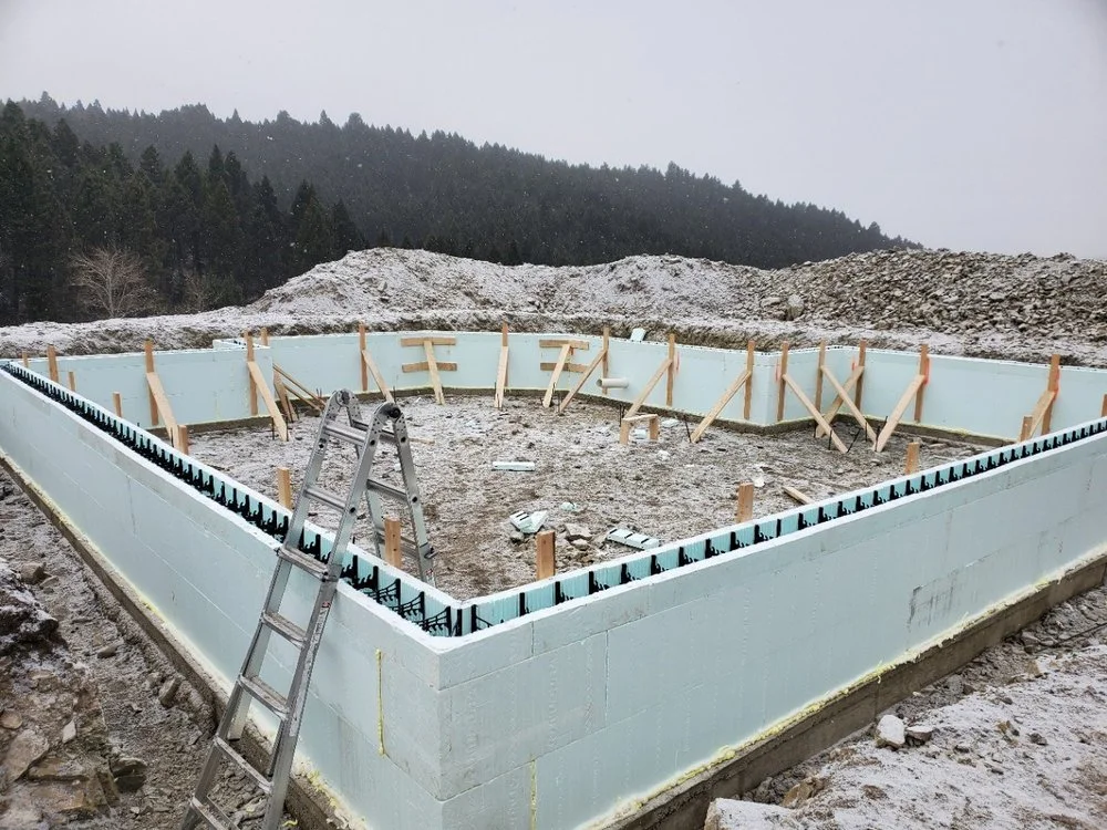Foundation with white foam insulation, drainage board, and wooden framing members on gravel base